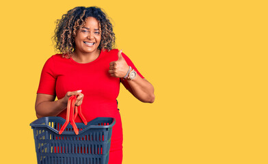 Young african american plus size woman holding supermarket shopping basket smiling happy and...