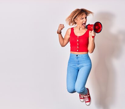 Young beautiful caucasian woman screaming using megaphone. Jumping over isolated white background