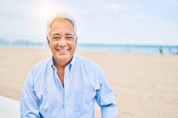 Handosme hispanic man with grey hair smiling happy at the beach, enjoying holidays on summer