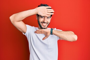 Young hispanic man wearing casual white tshirt smiling cheerful playing peek a boo with hands showing face. surprised and exited