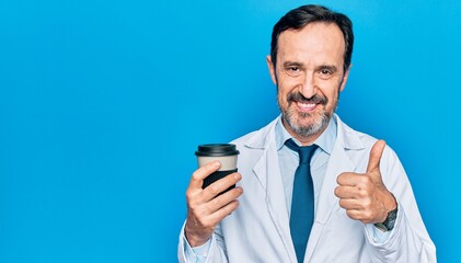 Middle age handsome doctor man wearing coat drinking cup of takeaway coffee smiling happy and positive, thumb up doing excellent and approval sign