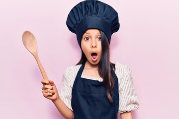 Fototapeta premium Beautiful child girl wearing cooker uniform scared and amazed with open mouth for surprise, disbelief face