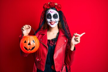 Woman wearing day of the dead costume holding pumpkin smiling happy pointing with hand and finger to the side