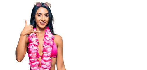 Beautiful hispanic woman wearing bikini and hawaiian lei smiling doing phone gesture with hand and fingers like talking on the telephone. communicating concepts.