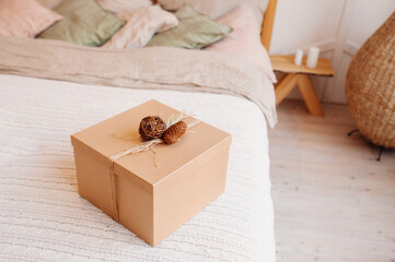 Obraz premium square Corton eco-friendly gift box decorated with pine cone and spruce twig on cozy bed with pillows, reusable packaging, selective focus