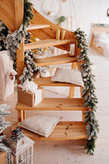 wooden staircase in the apartment is decorated with Christmas tree branches: soft and beige pillows, candlesticks and eco-friendly paper gift boxes. selective focus, vertical