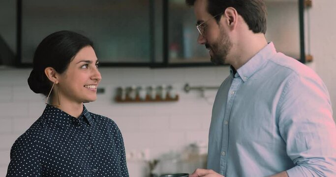 Diverse colleagues talk during break in office kitchen. Indian ethnicity woman communicates with workmate hold coffee cups enjoy pleasant conversation, discuss project. Good relations at work concept