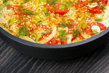 cooked fried omelet with herbs, spices and vegetables in a black pan on a wooden table