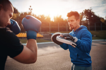 sport man boxer exercising in boxing gloves with personal trainer outdoor