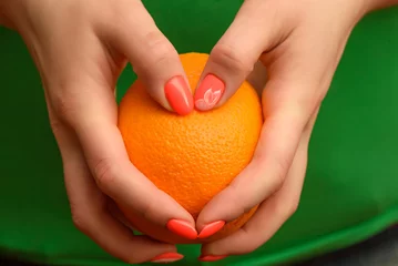 A girl with a beautiful orange manicure is holding a ripe orange in her hands. Close-up photo.