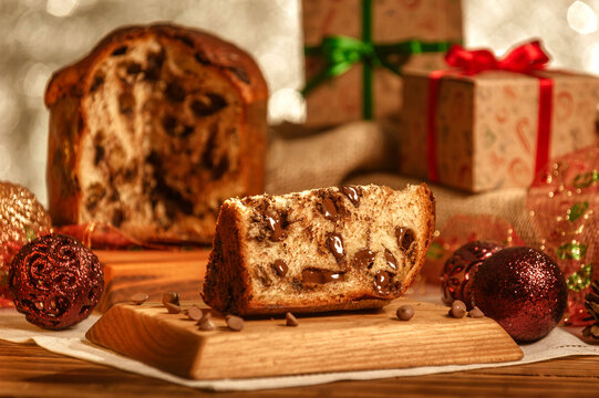 Slice of chocolate panettone  on wooden cutting board with christmas ornaments
