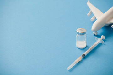 vaccine canister with syringe and white plane, blue background