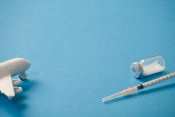 vaccine canister with syringe and white plane, blue background