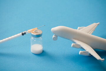 vaccine canister with syringe and white plane, blue background