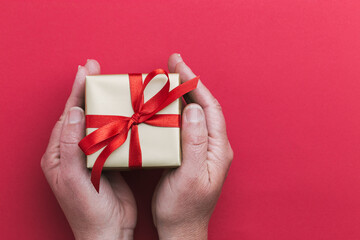 A small gold-colored gift box with a red ribbon in a woman's hands