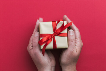 A small gold colored gift box with a red ribbon in a woman's hands