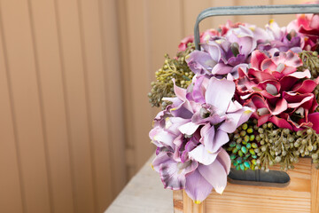 A bunch of colorful artificial flowers with violet, white, yellow and red petals in wooden box on the table was close-up short and selective focus with blurred background and copy space