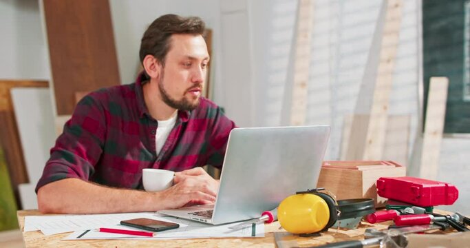 Young guy satisfied with interesting webinar on laptop computer about craft spending time in workshop during courses, skilled handyman checking ordering of clients on email via netbook