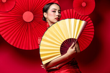 Beautiful Asian woman in traditional Chinese dress with colorful make up holding golden fan in ...