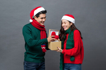 Happy surprised Asian woman opening Christmas gift box given by her boyfriend isolated on gray studio background