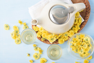 Hot chrysanthemum tea drink in glass cup with fresh flower on light blue background