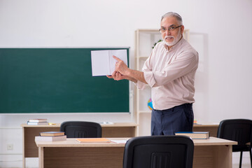 Old male teacher in front of blackboard