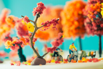 Side view miniature toy figurines of cyclist on a mountain bike in a park  in autumn, fall season or during cherry blossom season concept -  warm tone filter applied.