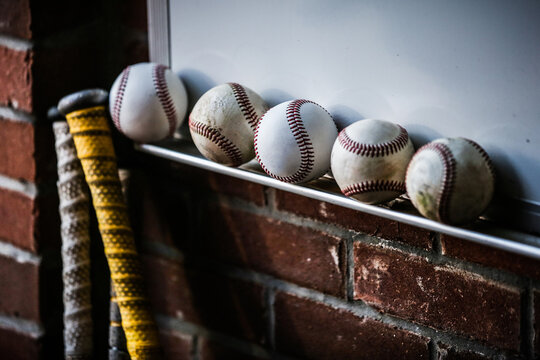 A line of five baseballs and a bat waiting in a brick dugout before a game