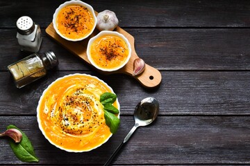 Pumpkin cream soup with fresh basil in bowl, napkin on wooden background. Top view. Copy space, flat lay. Menu, Food background. Healthy food concept.