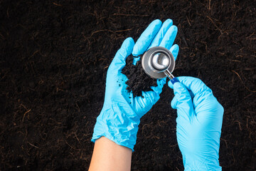 Hand of researcher woman wear gloves holding a stethoscope on fertile black soil for check...