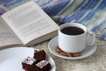 Winter. White coffee сup, chocolate cakes, almonds, warm blue sweater on a light background.