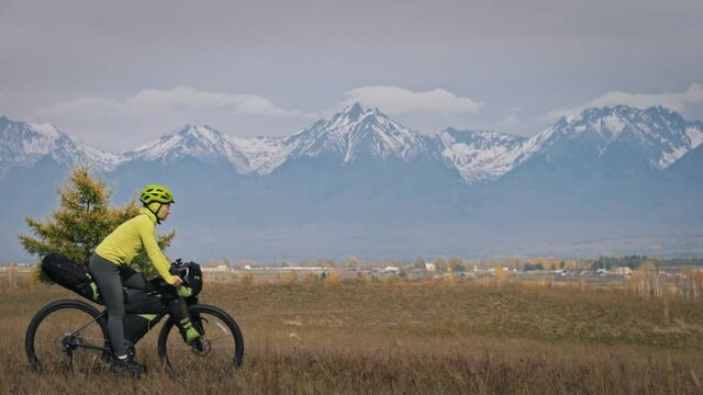 The man and woman travel on mixed terrain cycle touring with bikepacking. The two people journey with bicycle bags. Sport bikepacking, bike, sportswear in green black colors. Mountain snow capped.