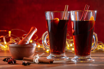 Two glasses of christmas mulled wine with spices on wooden table against illumination light.