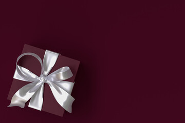 Crimson gift box 3d with silver ribbon and bow on Crimson background