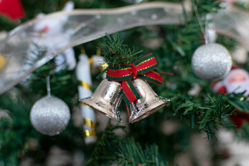 Various Christmas decorations on a Christmas tree. A pair of silver bells next to Christmas balls.
