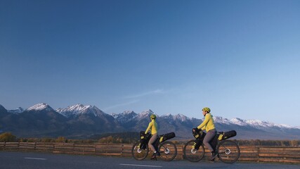 The man and woman travel on mixed terrain cycle touring with bikepacking. The couple journey with bicycle bags. Mountain snow capped.