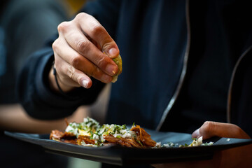 Men squeezing lime into shepherd's taco indoors, close-up