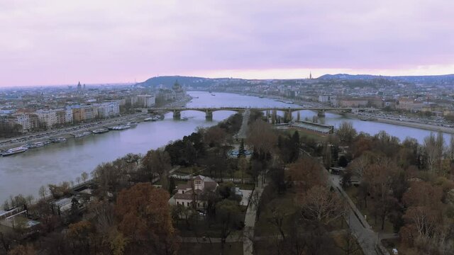 Autumnal Trees In Margaret Island With Arpad Bridge At Danube River In Budapest, Hungary - drone pullback