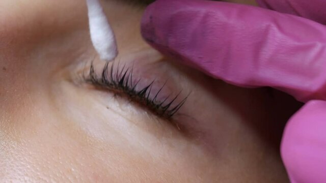 Face of young girl before eyelash lamination procedure in a professional beauty salon. The master washes off the black paint on the eyelashes during the eyelash curling procedure with a special brush.