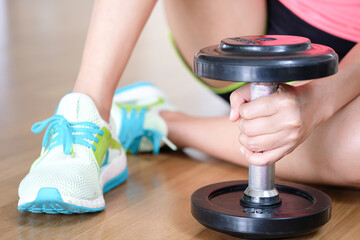 Woman exercise by personal trainer at gym and then be tired. She sit on floor for rest that dumbbell in front of her. Women wearing sport shoes.