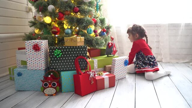 Little girl sorting out christmas gifts near christmas tree