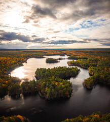 Obraz premium Beautiful aerial photograph of Kingston Lake in upper Michigan with beautiful sunny sky and clouds over the forest of fall foliage covered trees and evergreens and meandering water in the lake below.