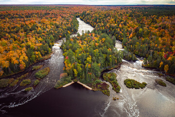Beautiful aerial of the lower waterfall cascades on the Tahquamenon River surrounded by evergreen and fall foliage colored deciduous trees with yellow, green, red and orange leaves in Upper Michigan. - Powered by Adobe