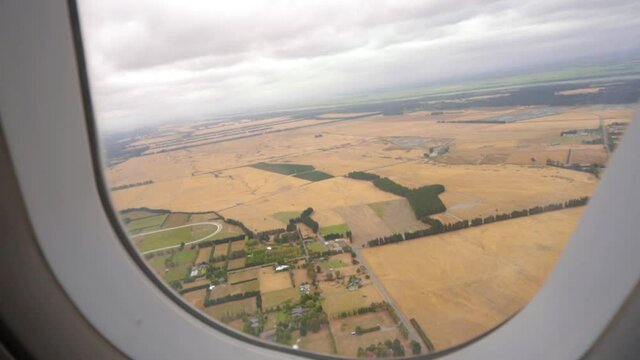 Slow motion push in of plane window as plane flies over farmlands in drought and dry grass