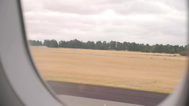 Slow motion handheld shot looking out of plane window at runway with dry grass and trees in background