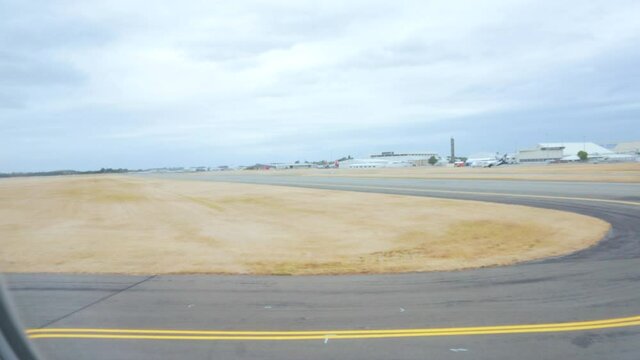 Slow motion shot looking out of plane window with runway and airport in background on dark gloomy day