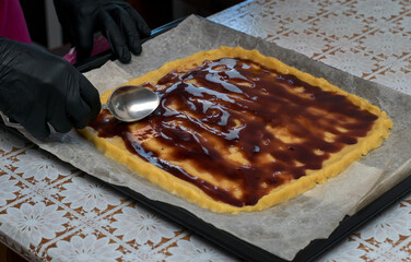 Spread the jam on top of the prepared dough on the kitchen table with a spoon.