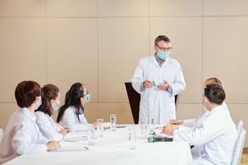 Mature doctor in medical mask showing coronavirus vaccine to young colleagues and explaining its working principle