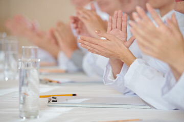 Close-up image of medical workers clapping after speech of colleague at conference