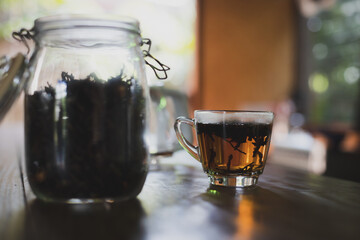 Cup of hot tea and dry tea leaves in a glass bottle put on the table in the kitchen in the morning time.